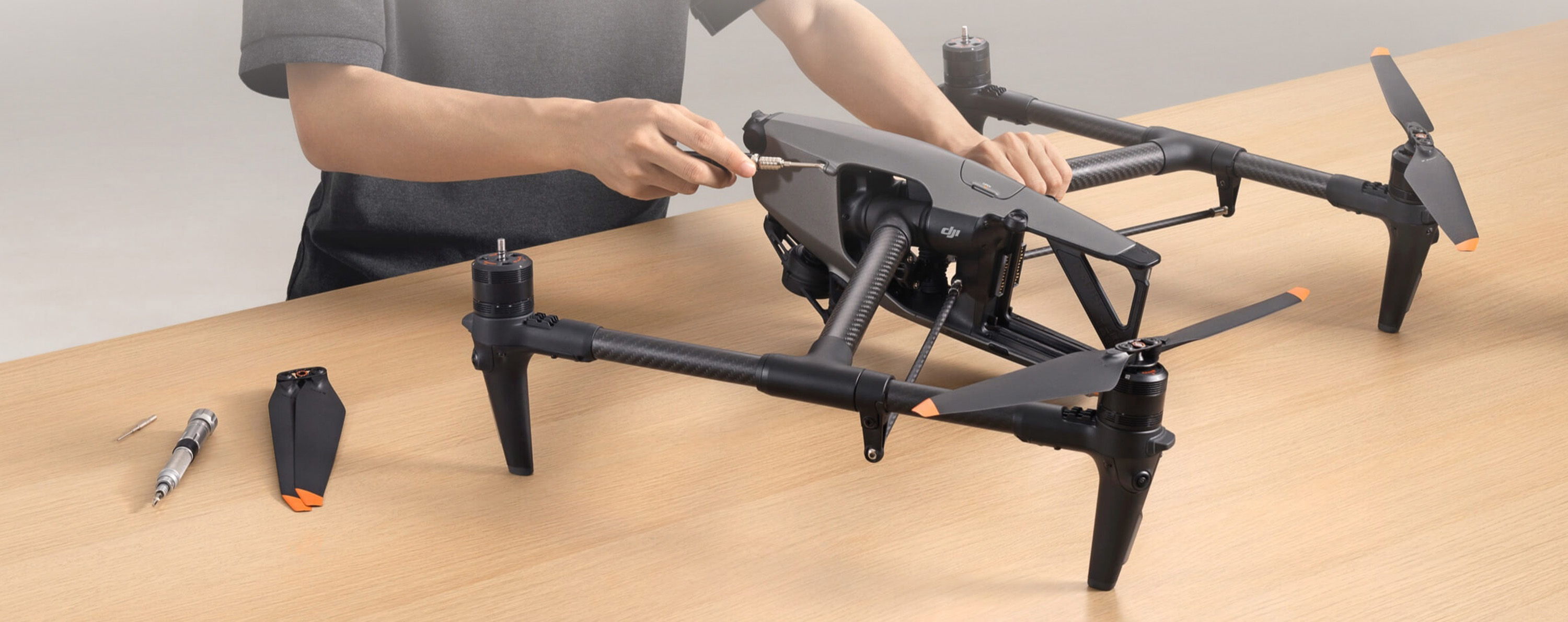 Person assembling a DJI Inspire 3 drone on a wooden table with tools.