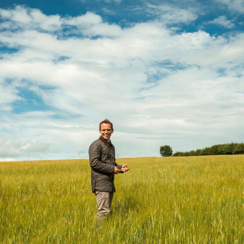 Felix James, co-founder of Small Beer, standing in a barley field on a sunny day