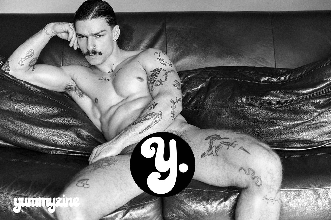 Black and white photo of a tattooed man reclining on a couch.