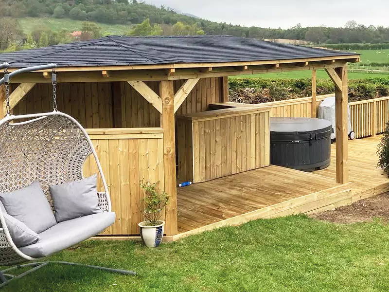 An image of a deck, hot tub, pergola and outdoor swing in a person's garden. 