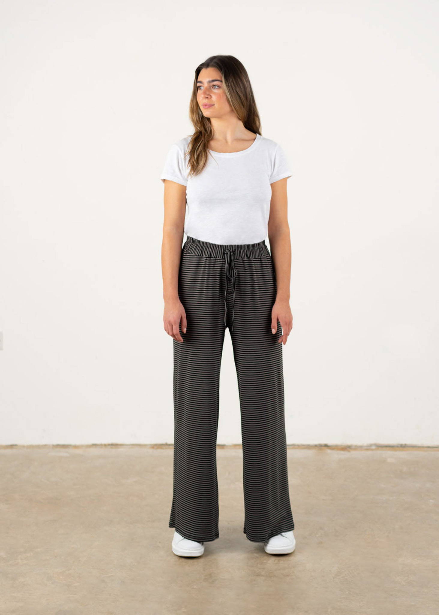 A model wearing a white short sleeve t shirt with khaki and black wide leg jersey trousers and white trainers