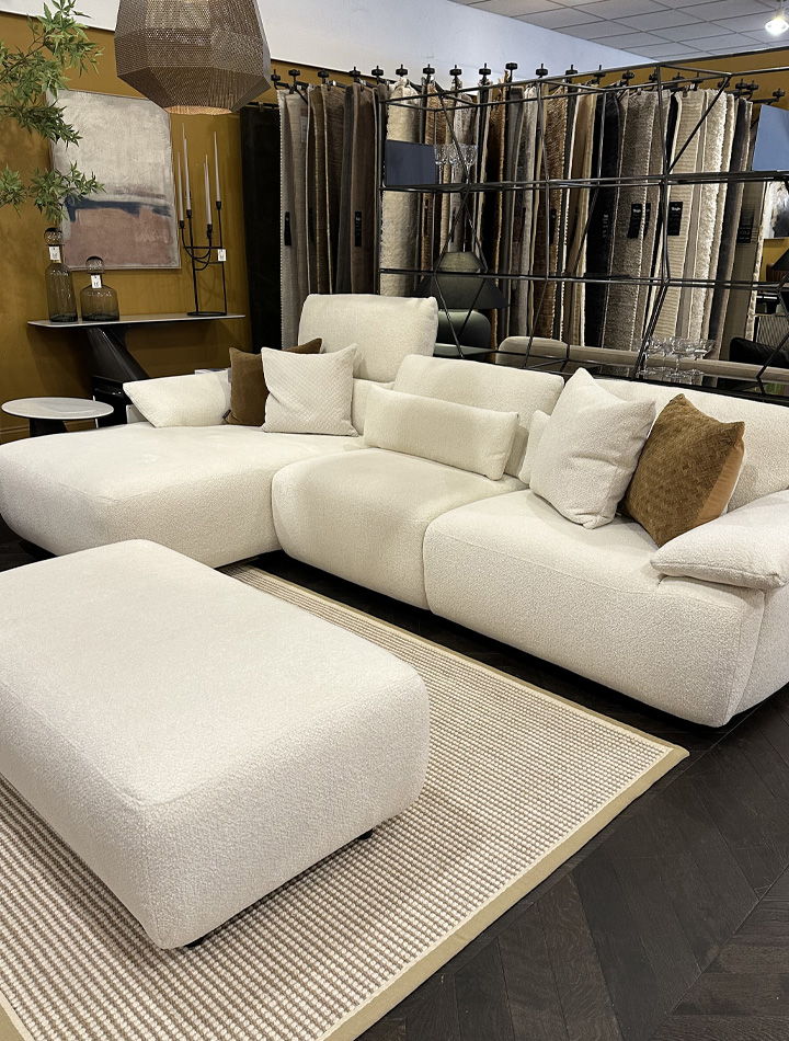Modern white sectional chaise sofa with cushions and an footstool on a rug.