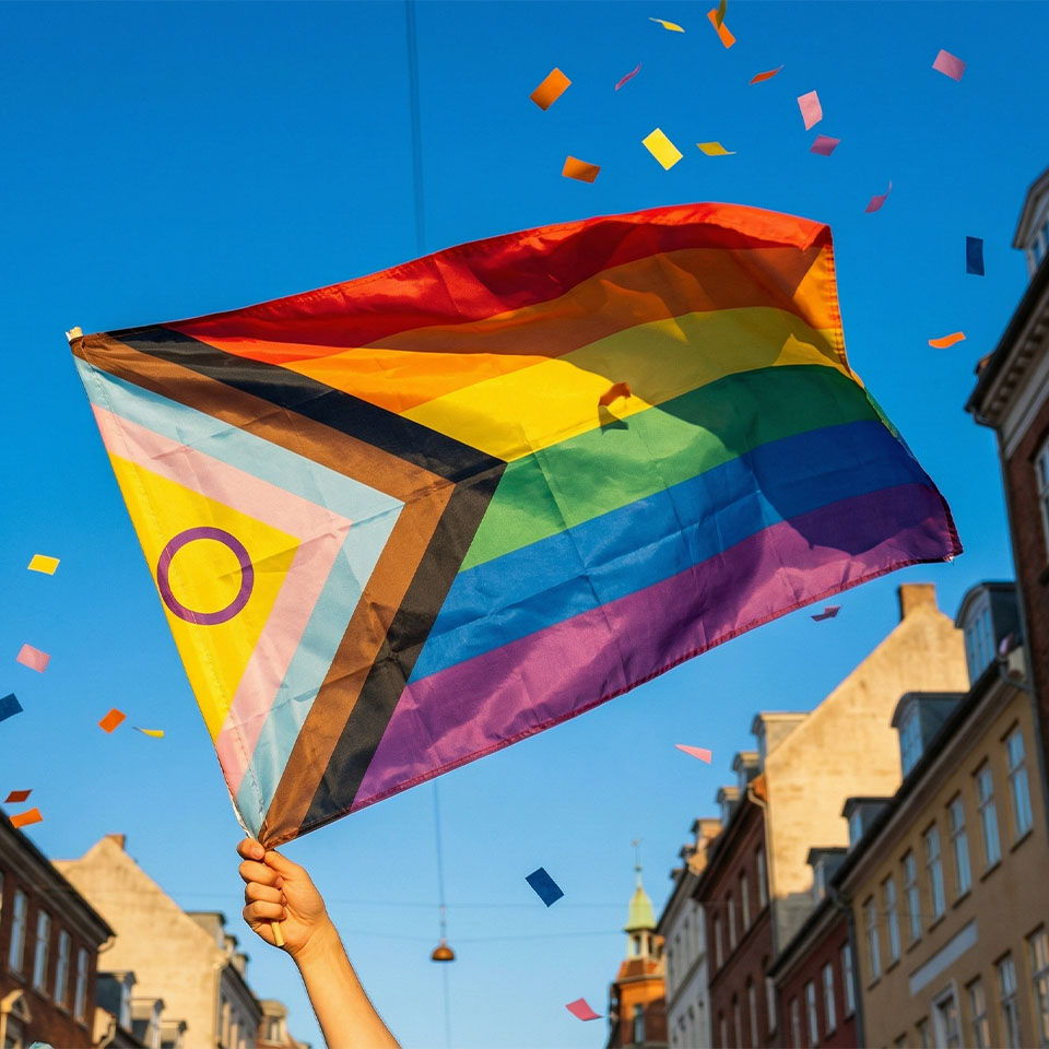 Hand holding a rainbow flag with confetti and blue sky background.