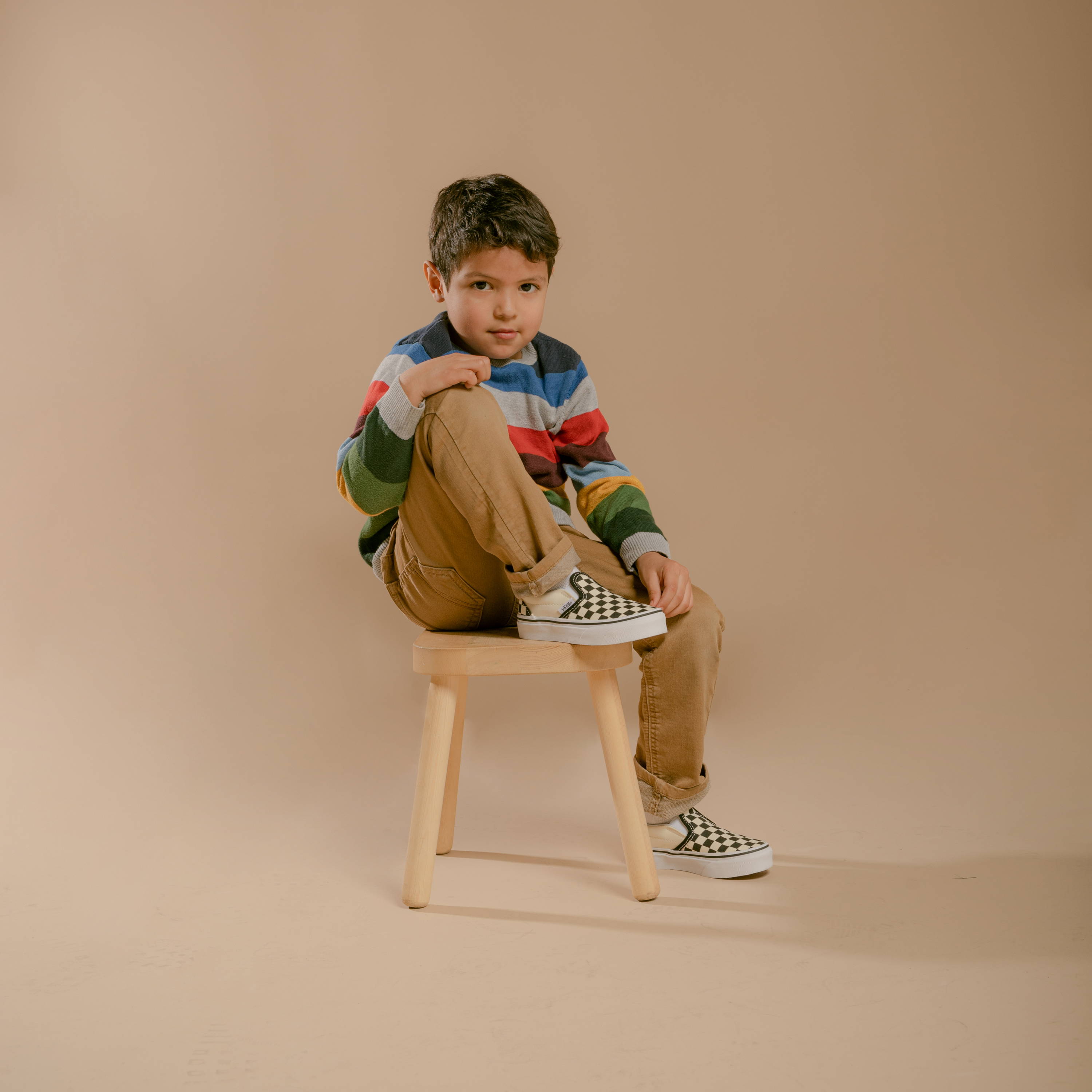 young boy sitting wearing checkered vans