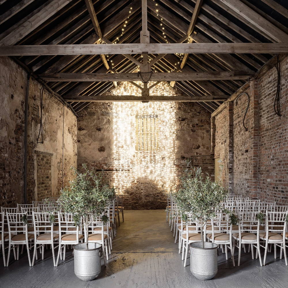Hanging warm white fairy lights on a wall in a barn with guest seats facing the front.