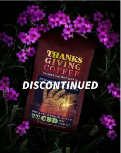 CBD Coffee bag in the grass with purple flowers around it  with the words Discontinued  written over it