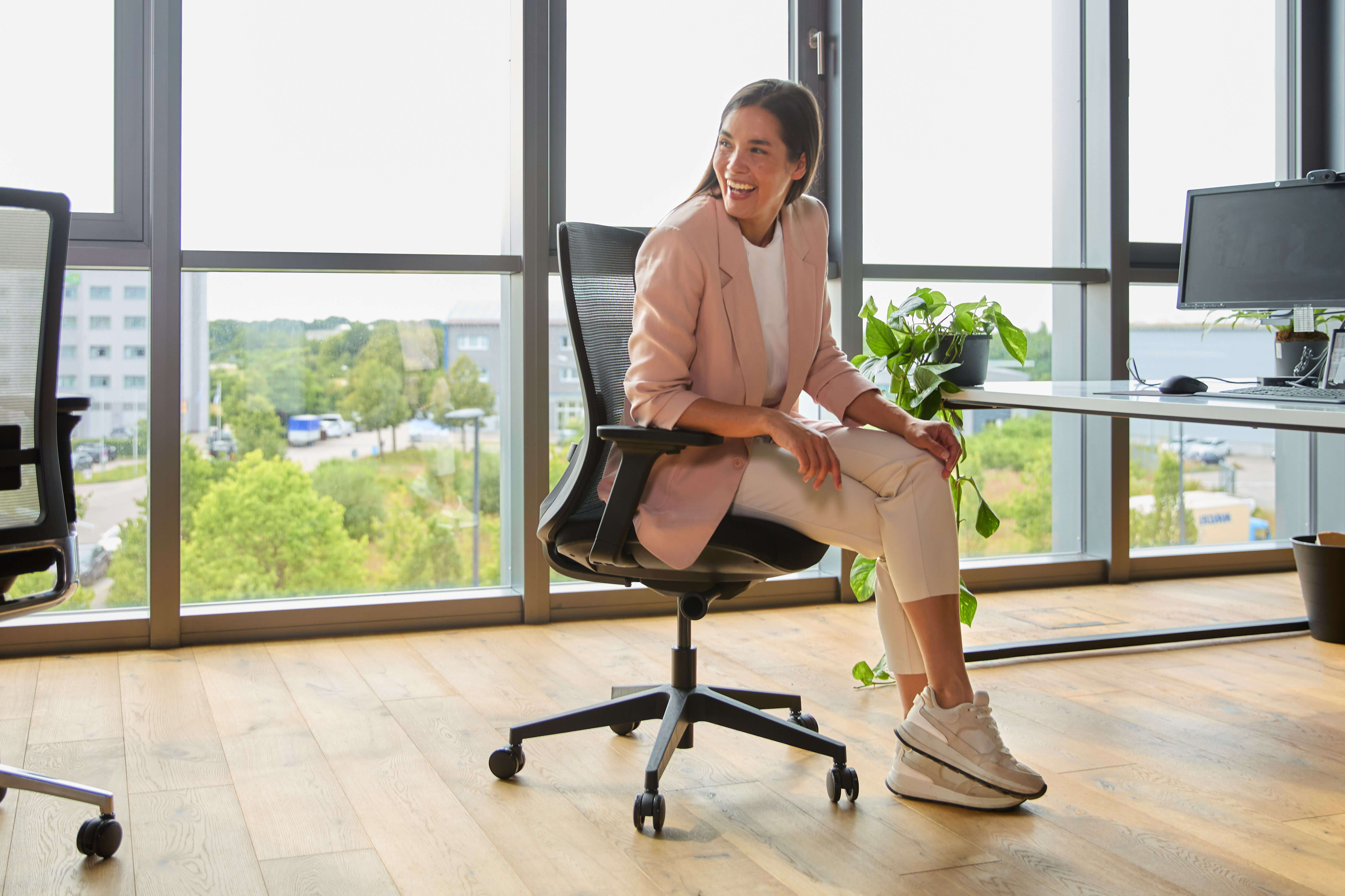 A woman sits in a Ergo ofinto Ergo office chair in a modern open-plan office