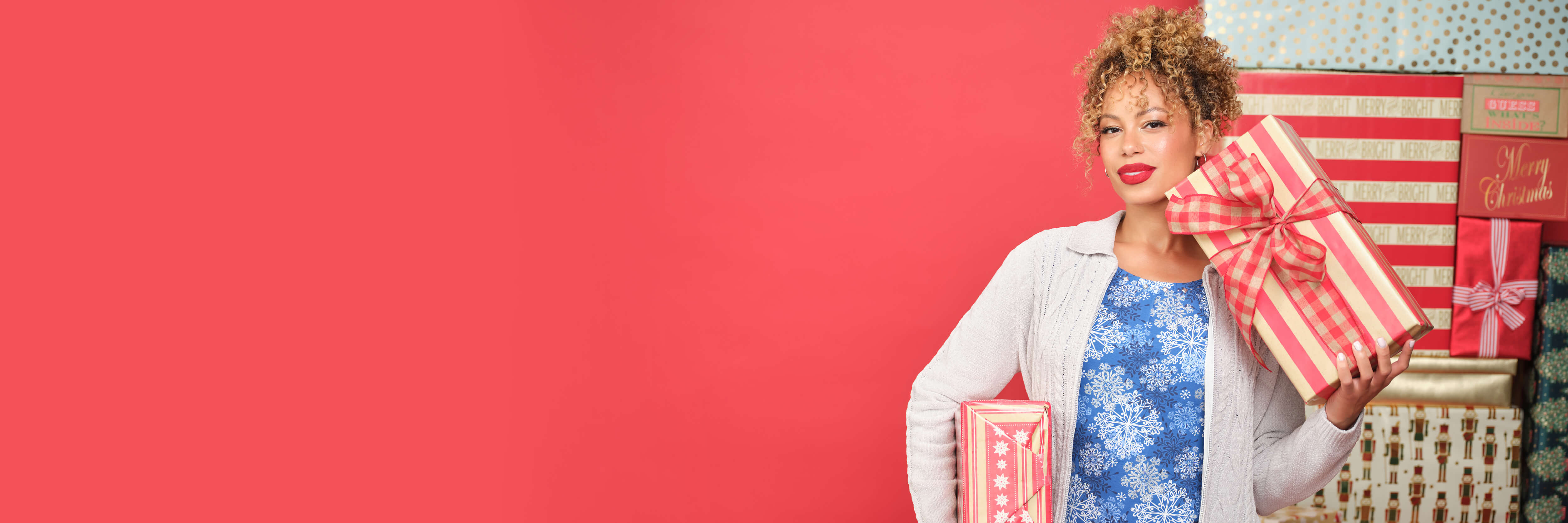 Woman holding gifts against a vibrant pink background, smiling confidently.