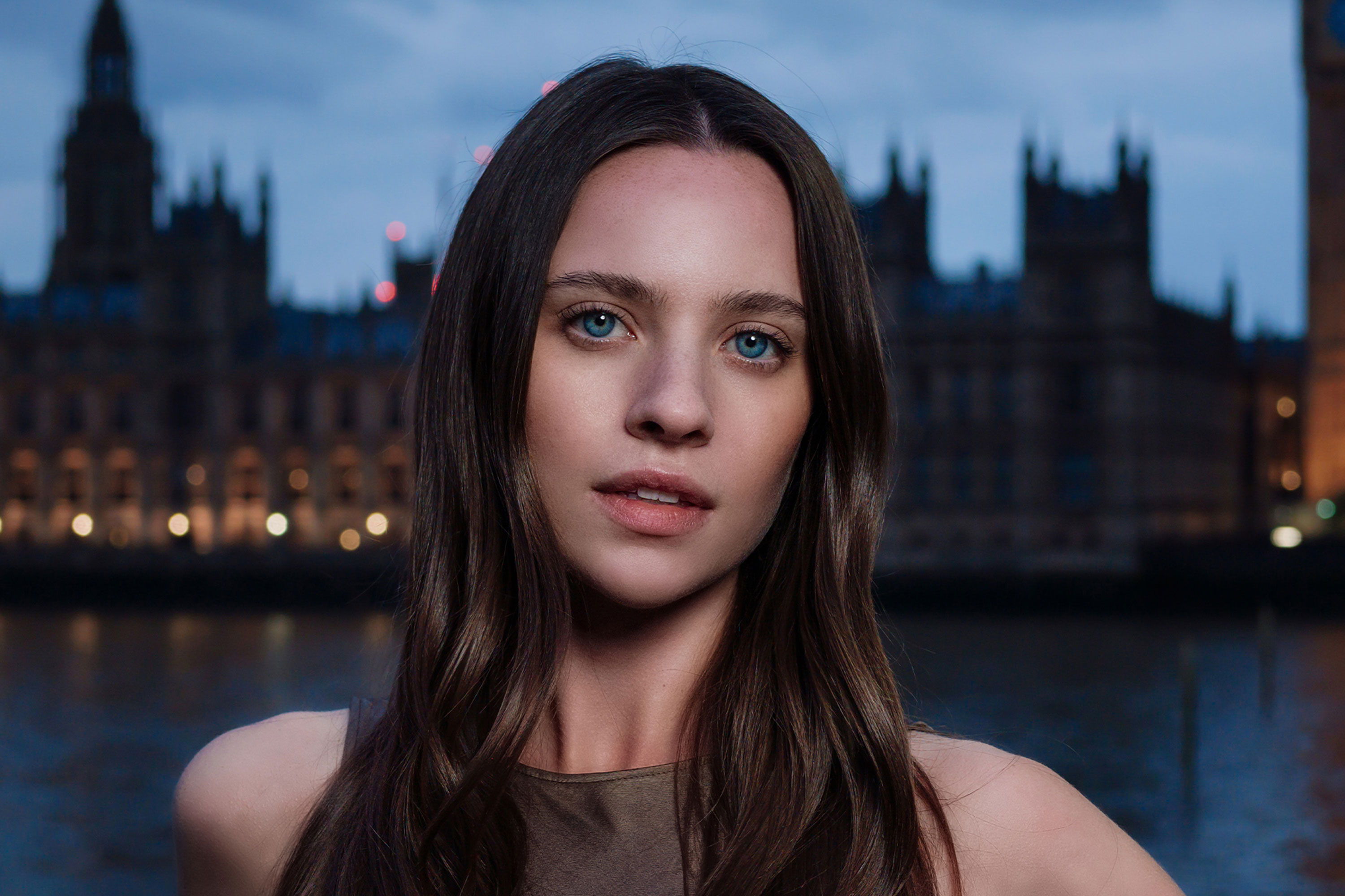 Woman with long hair in front of a cityscape at dusk.
