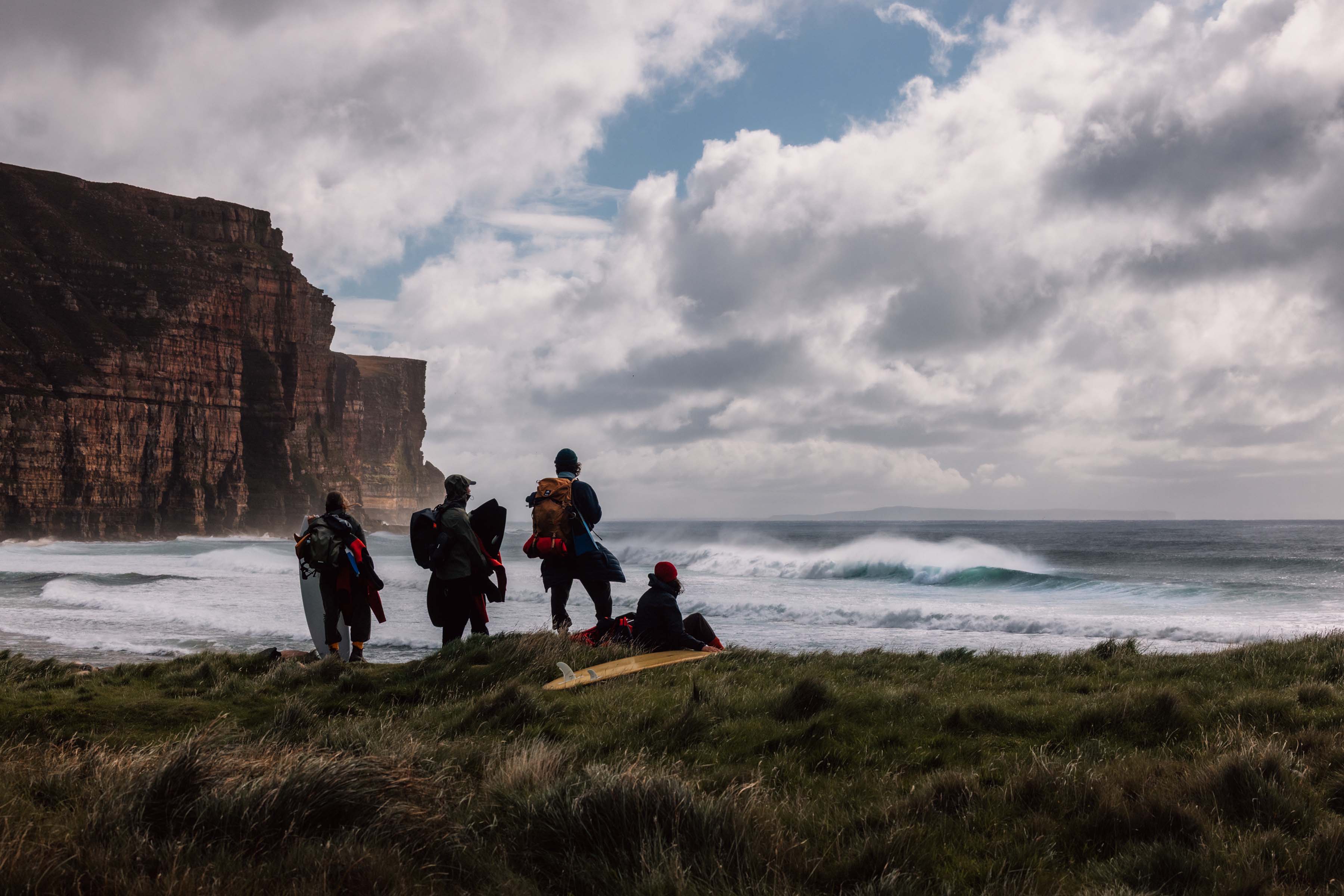 People standing near the ocean with cliffs and clouds in the background.