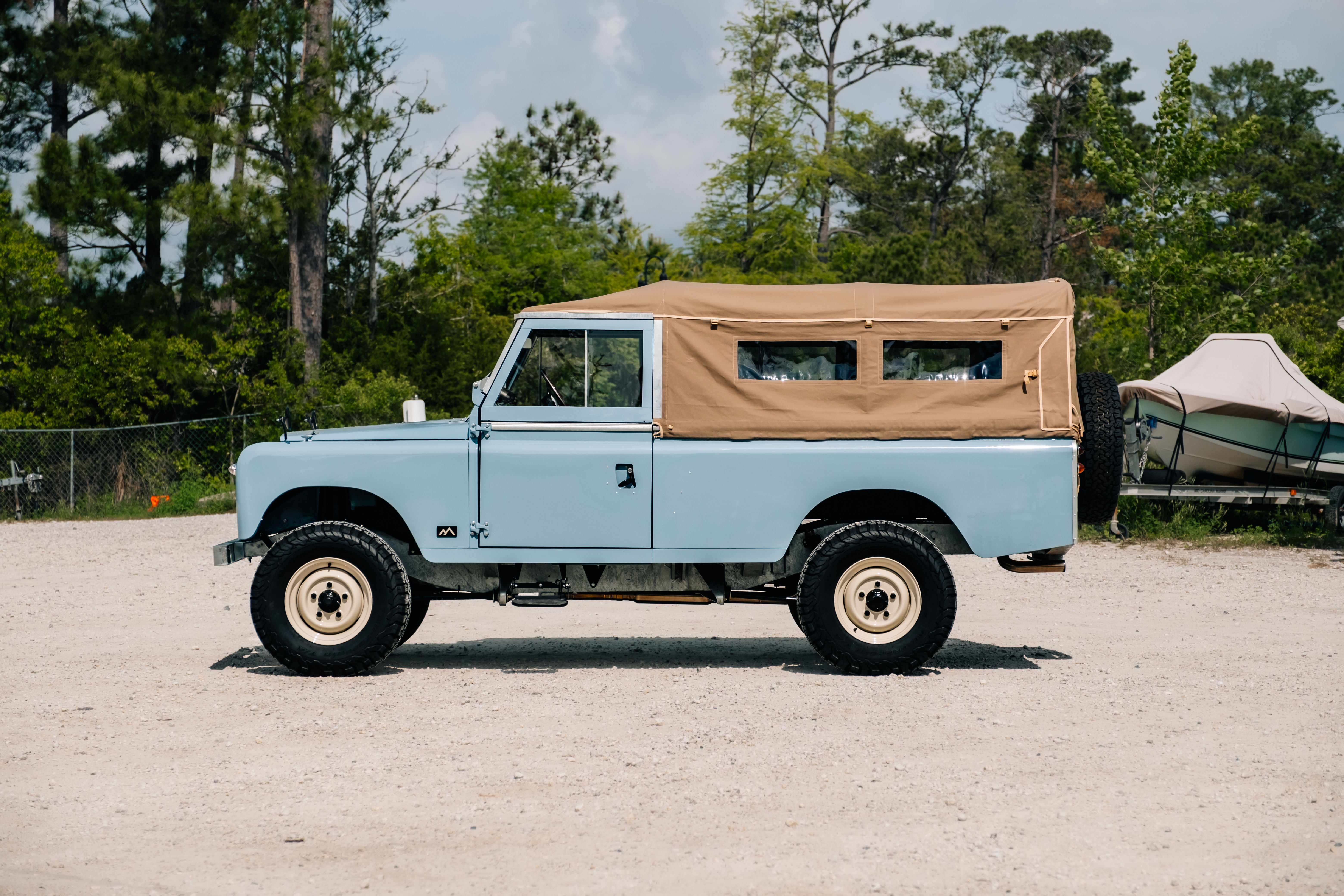 Light blue vintage truck with a tan canvas top parked on gravel.