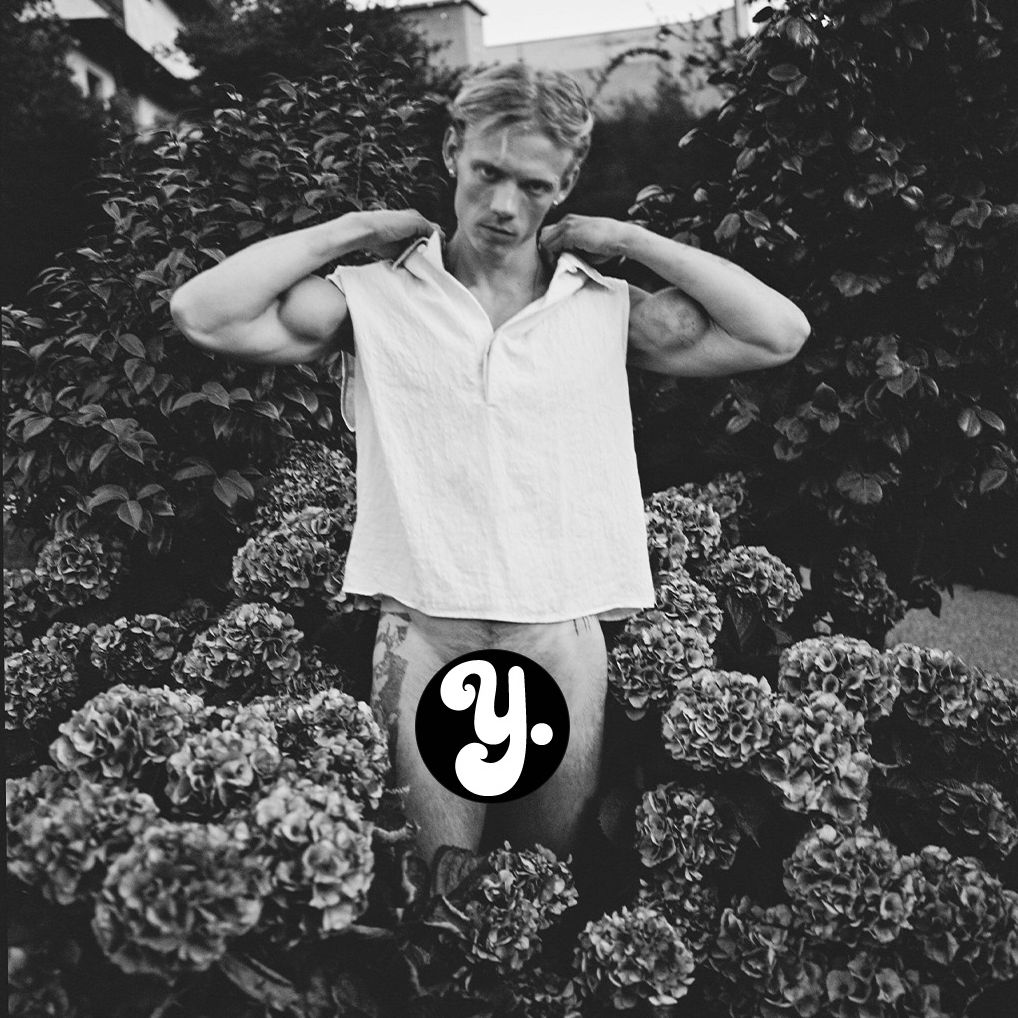 A man adjusting his shirt surrounded by flowers in black and white.