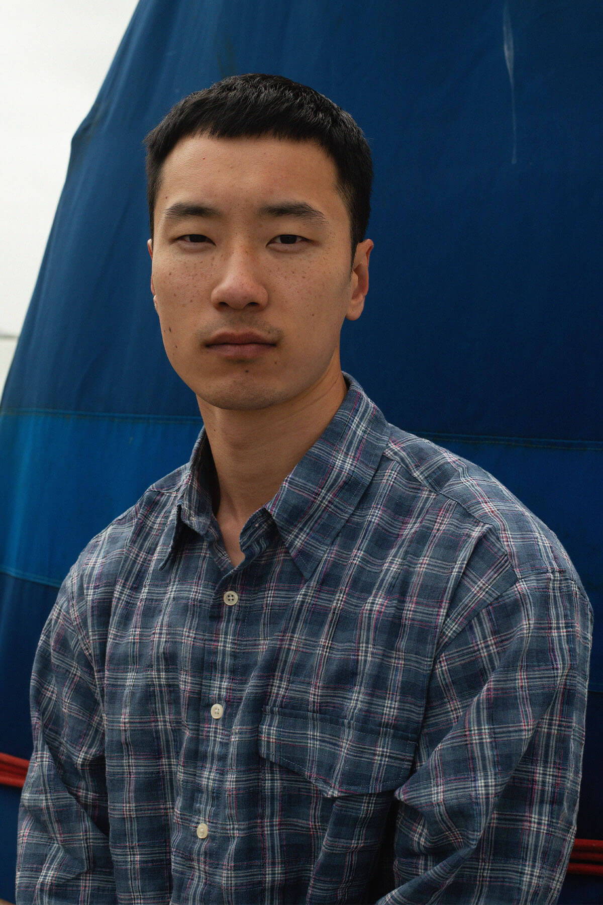 A person in a plaid shirt standing in front of a blue background.