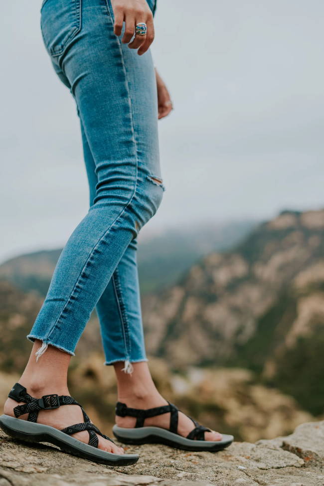 woman standing on rock cliff with jeans and sport sandals