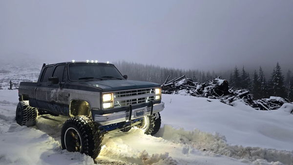 Snowy mountain view of Joseph's lifted 1985 Chevy K30 with the lights on, install photo 2