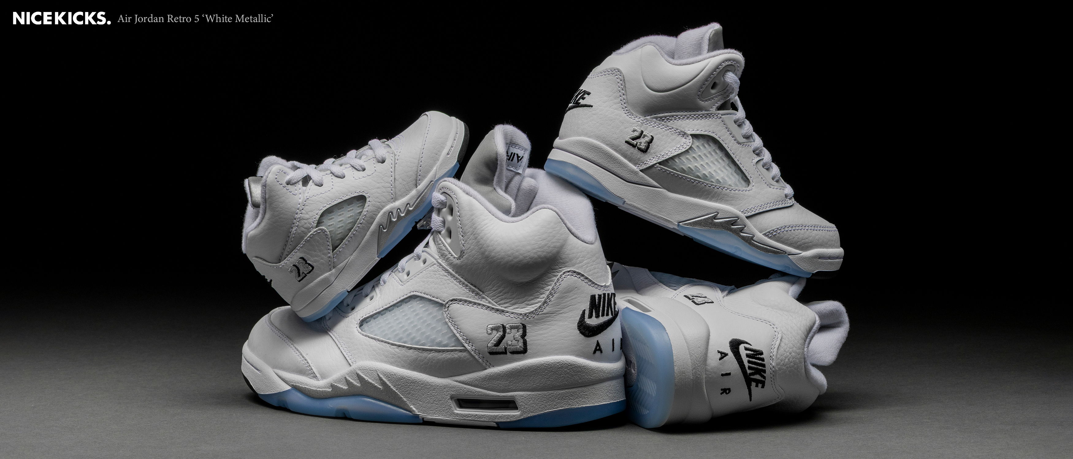 A collection of white sneakers stacked on a dark background.