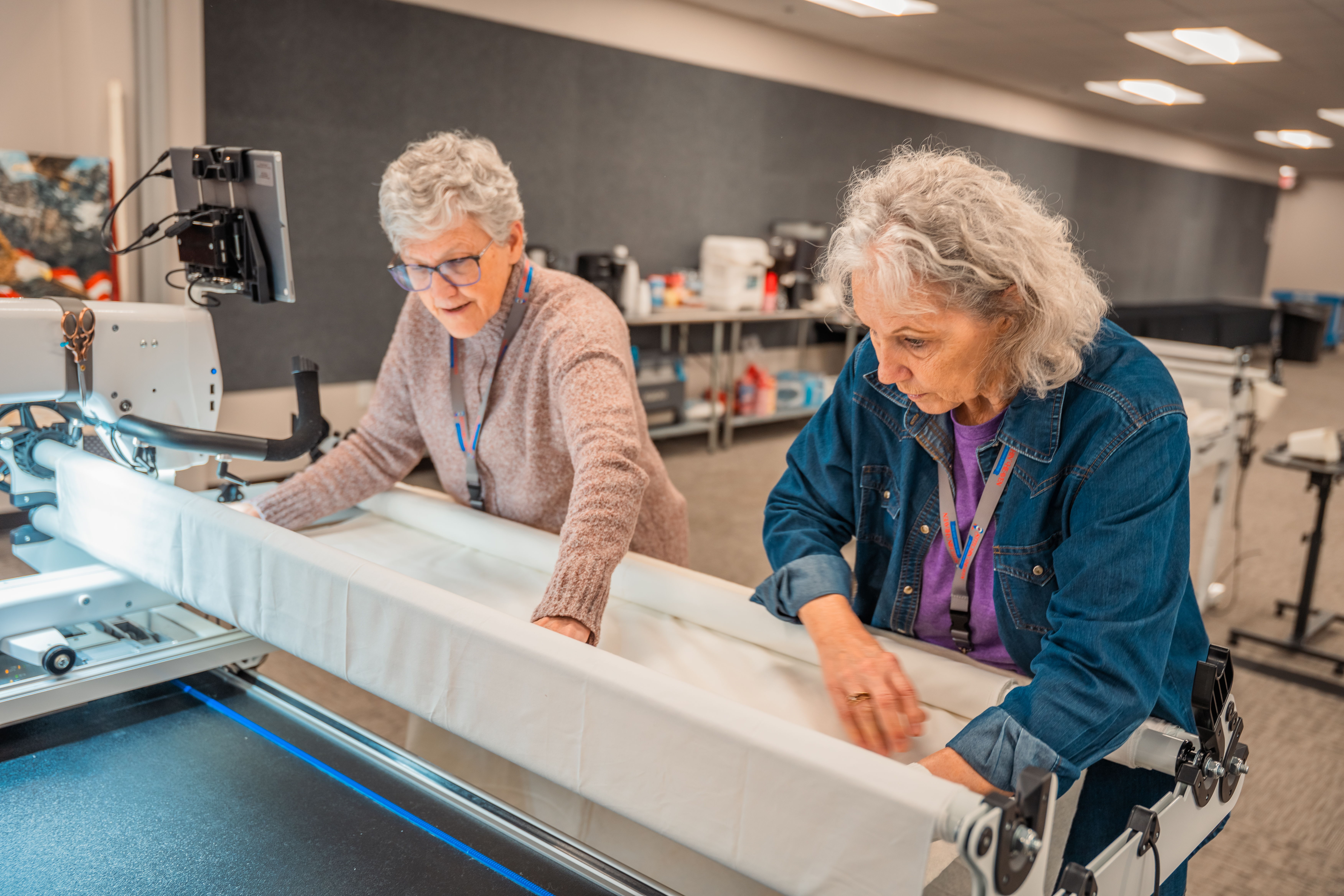 Two women working on a quilting machine in a bright workshop.