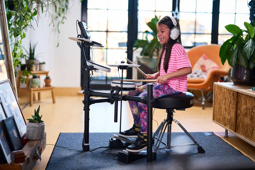Girl playing an electronic drum set in a bright, modern room.
