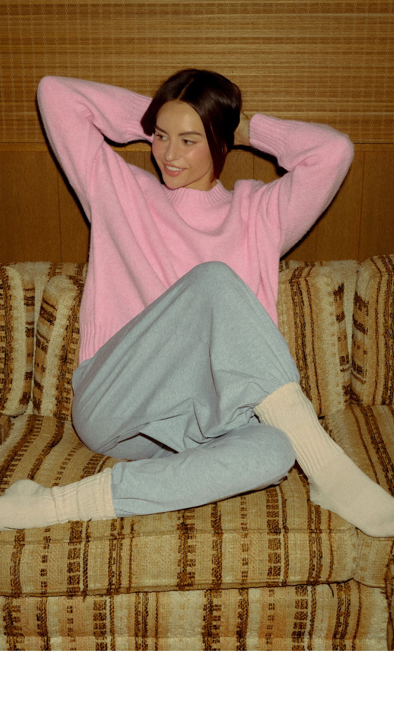Young woman in pink sweater sitting on couch, relaxed pose.