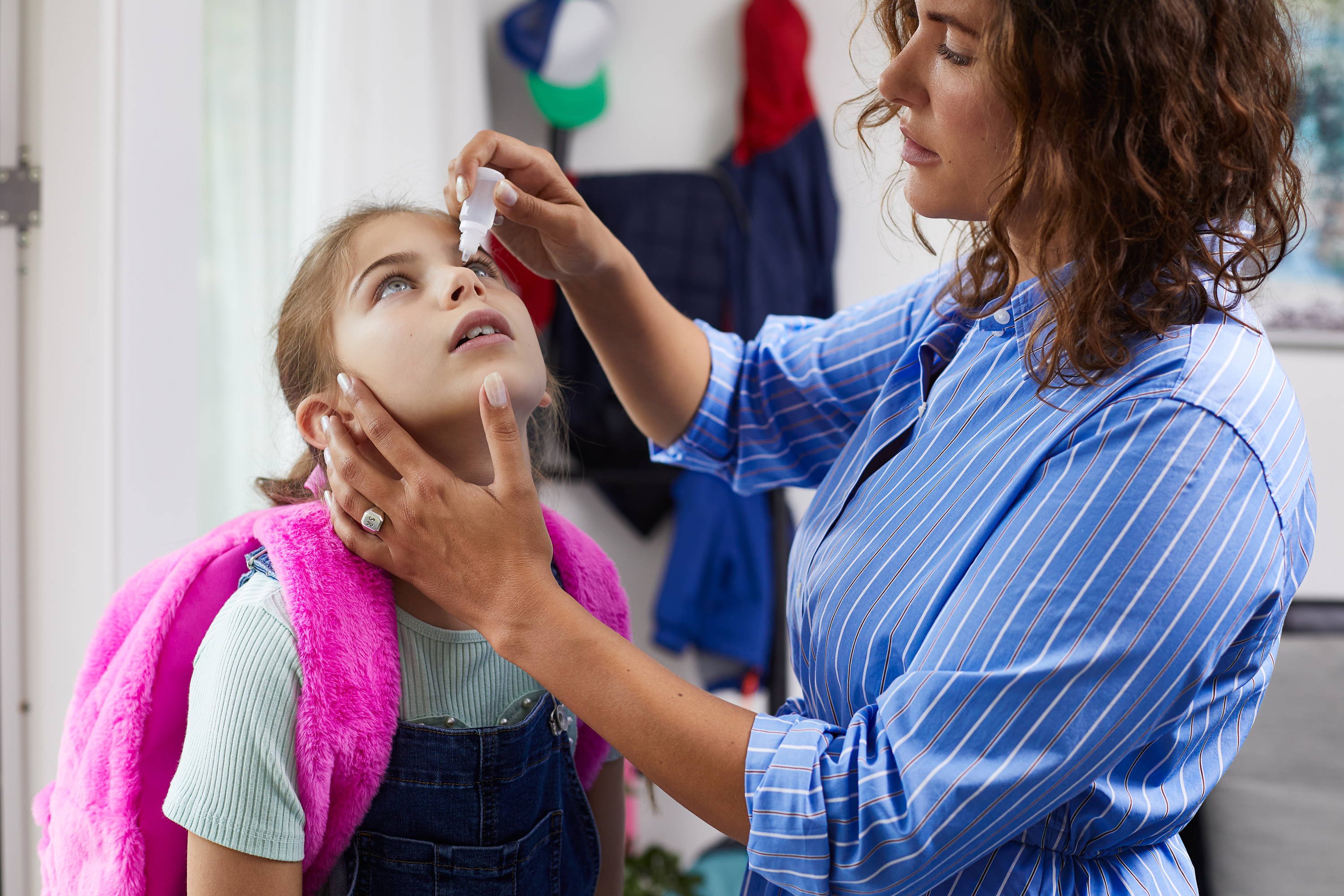 Een meisje krijgt van haar moeder allergie oogdruppels tegen de jeuk in haar ogen.