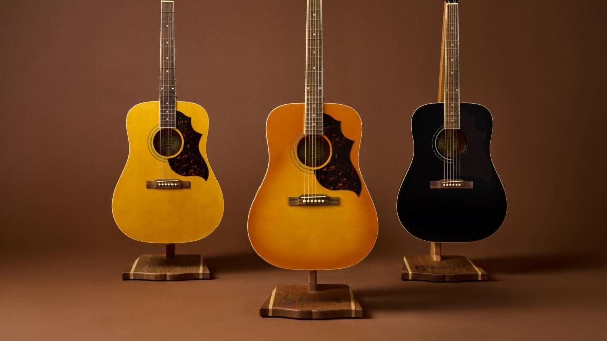 Three acoustic guitars in various colors displayed on stands.