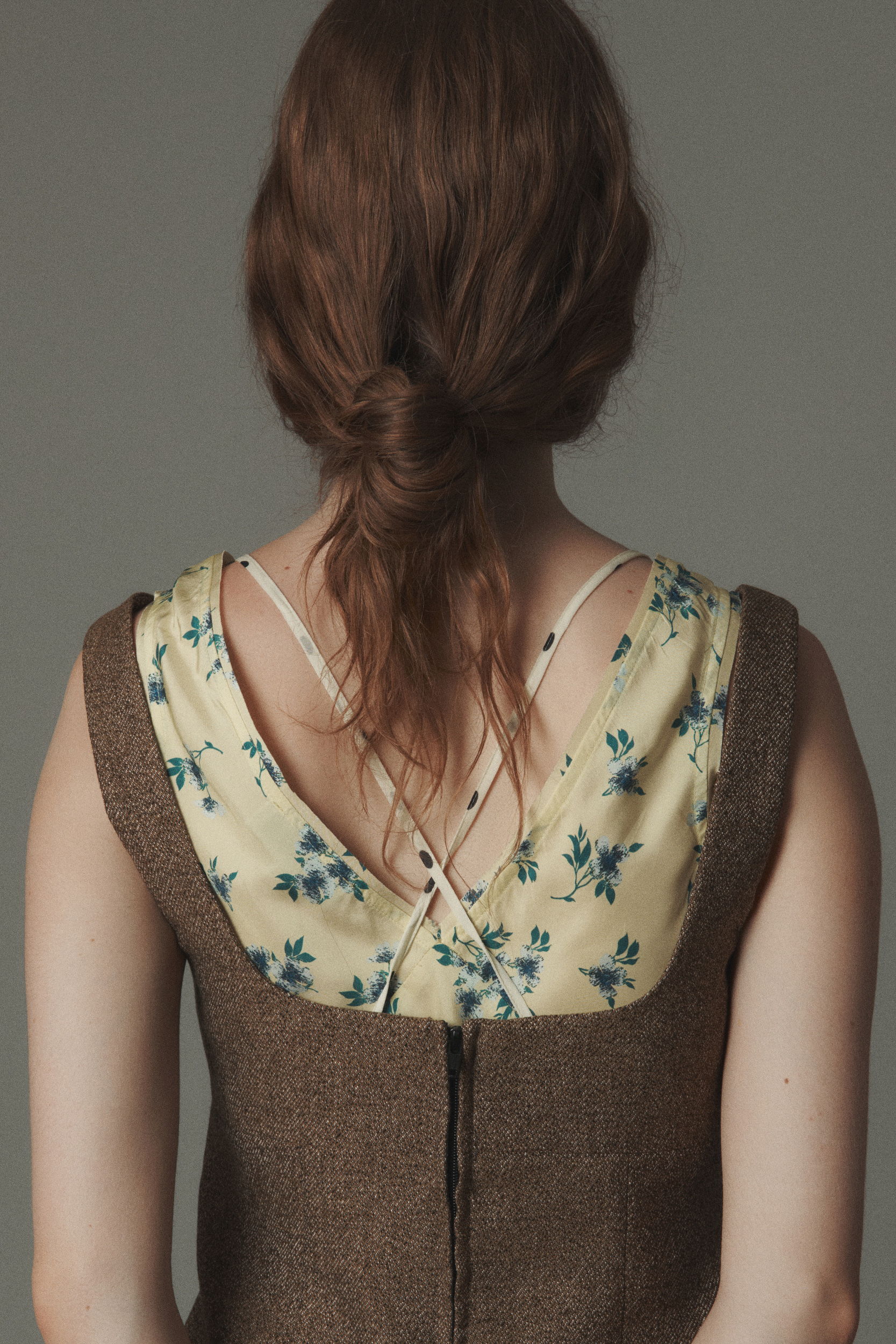 Back view of a woman wearing a floral dress with a brown overlay.