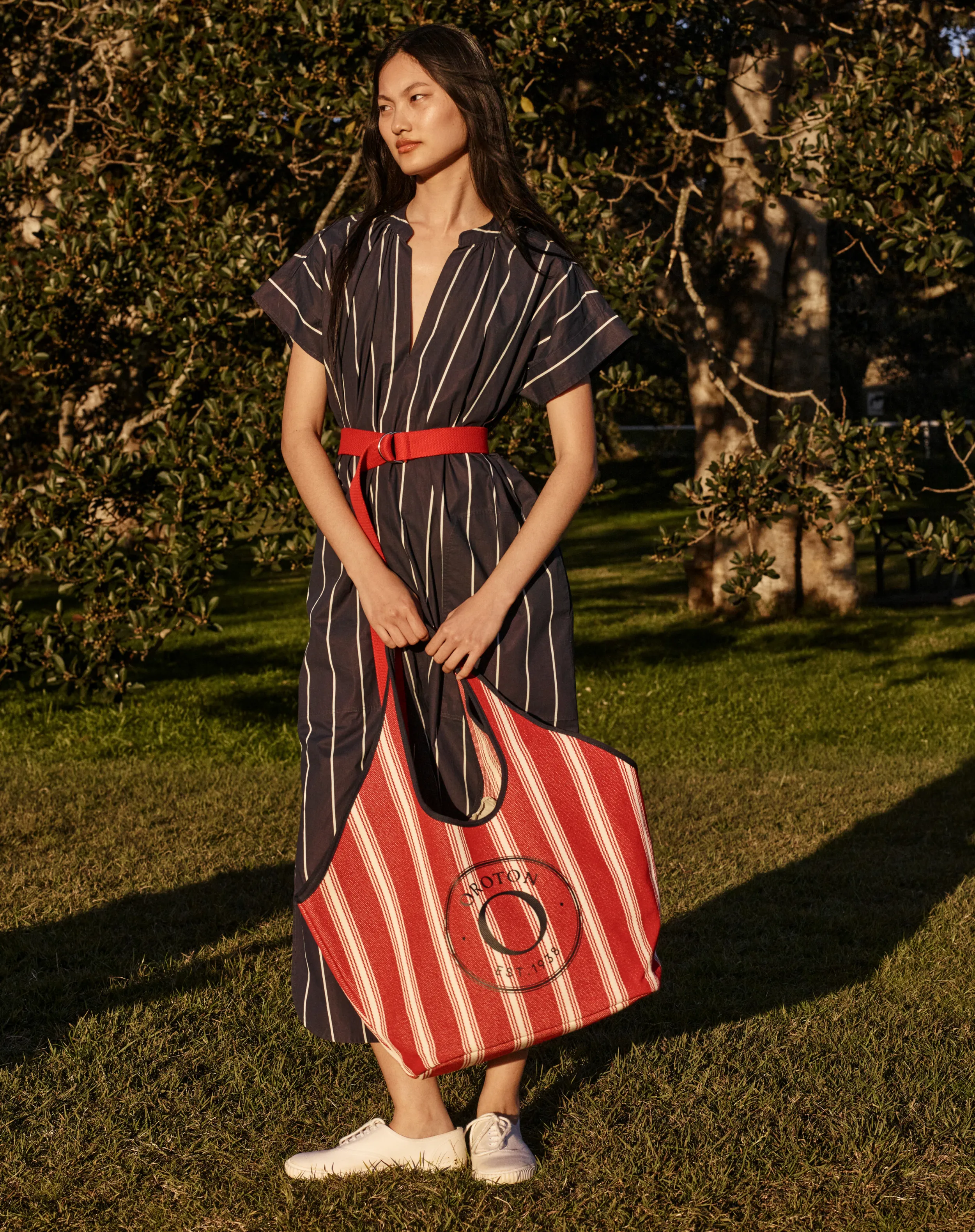 Woman in a striped dress holding a red and white bag outdoors.