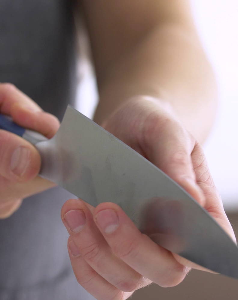 A chef holding a knife blade edge up to inspect for damage along the cutting edge. 