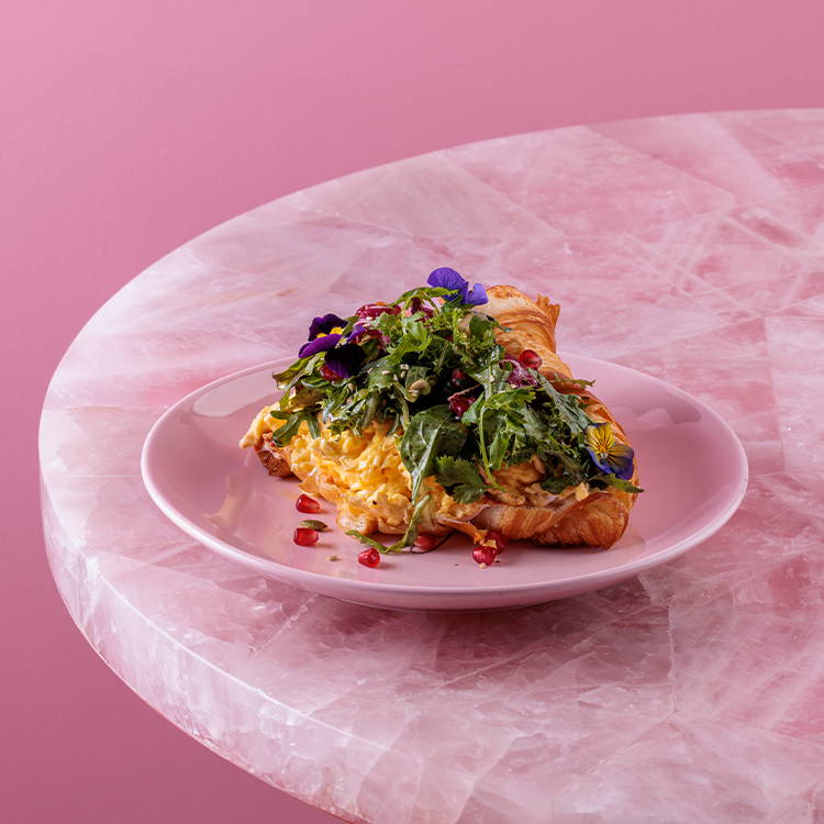 Loaded croissant with scrambled eggs and salad on pink plate