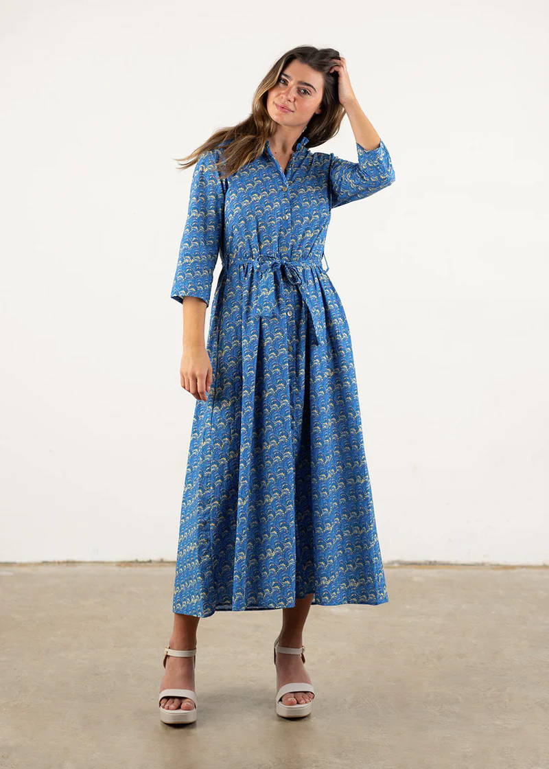 A model wearing a blue dress with a filagree yellow pattern, 3/4 sleeves and belted waist with cream chunky heels