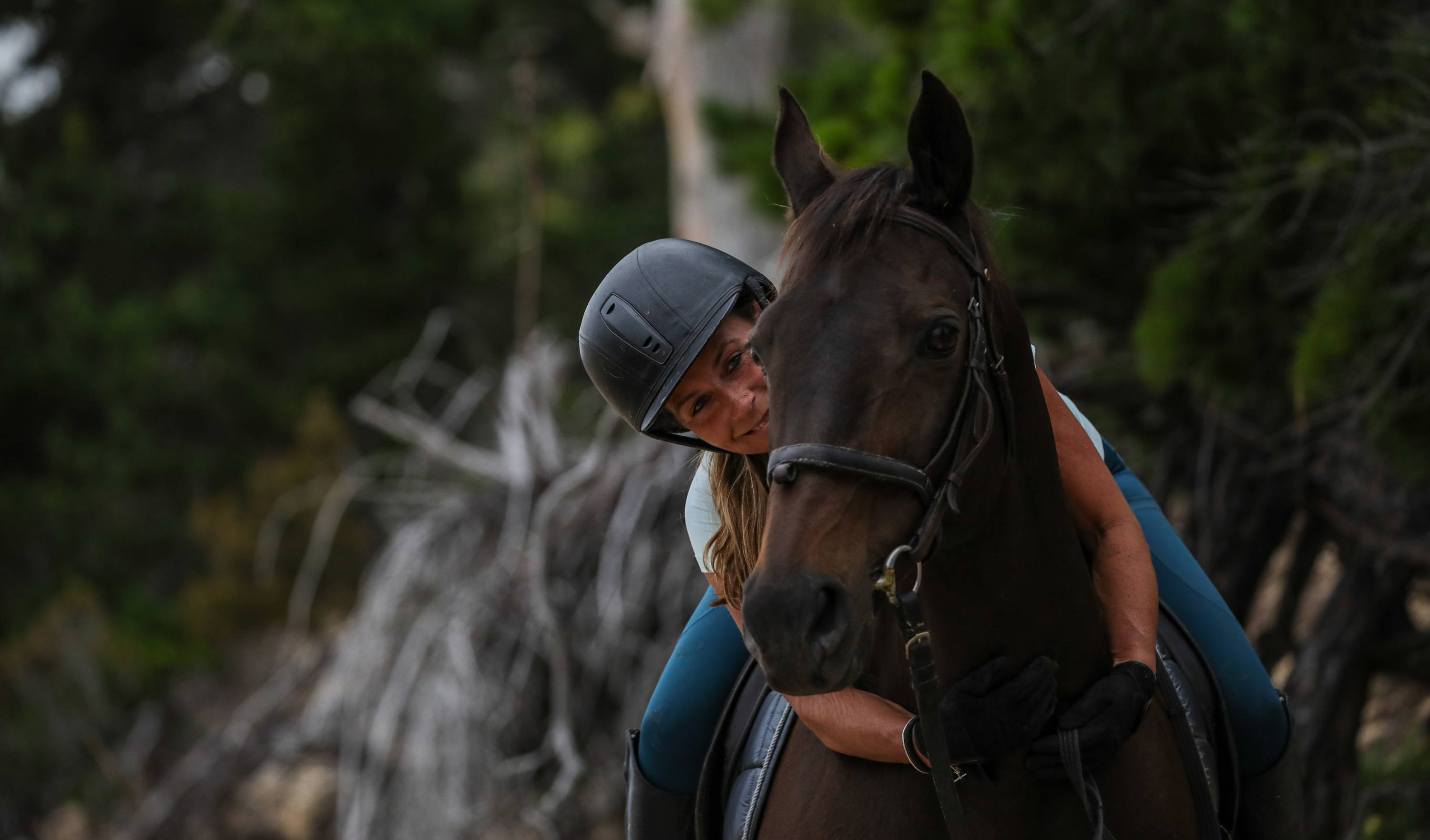 A rider leaning close to a horse in a natural setting.