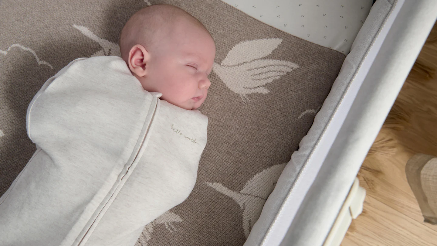 A sleeping baby wrapped in a white blanket on a patterned rug.