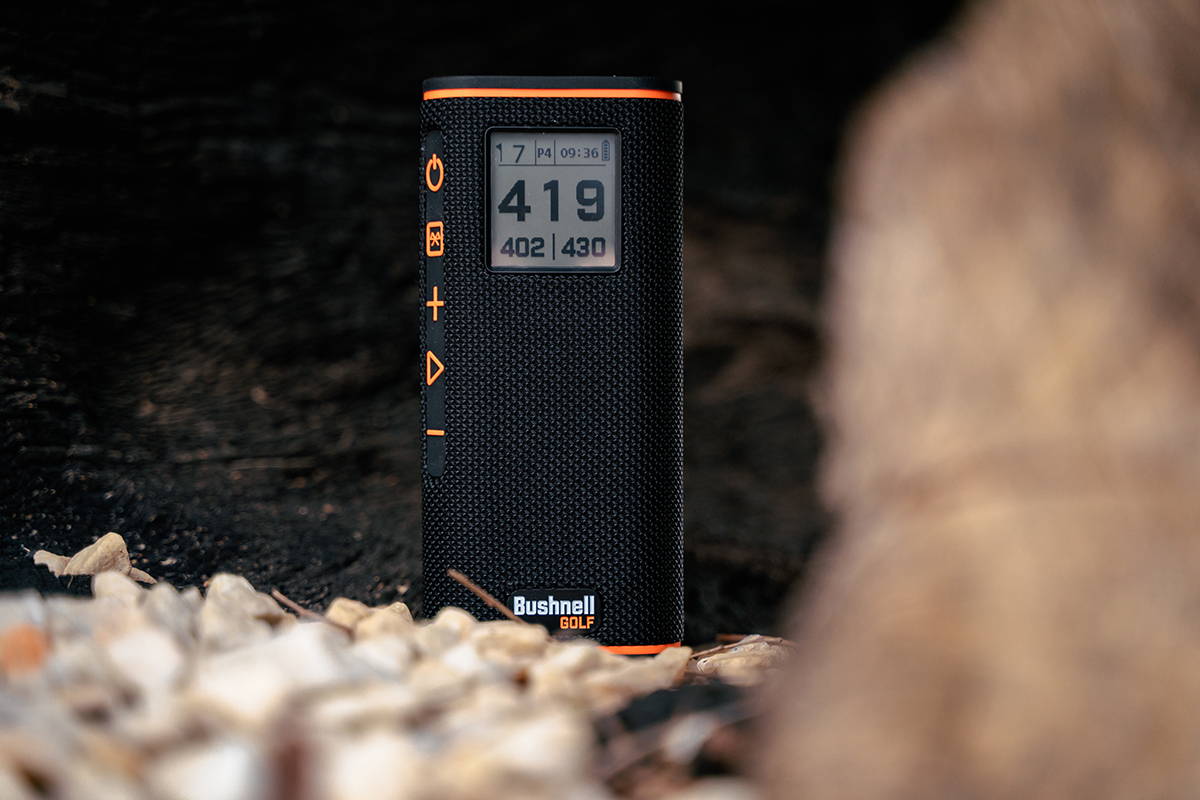 The Bushnell Wingman View golf speaker standing in some rocks showing GPS distances on the LCD screen