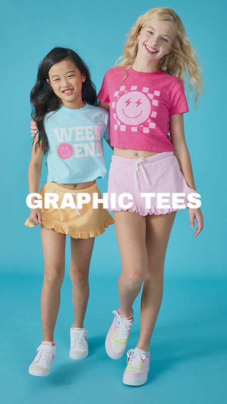 Two girls in colorful graphic tees smiling against a blue background.