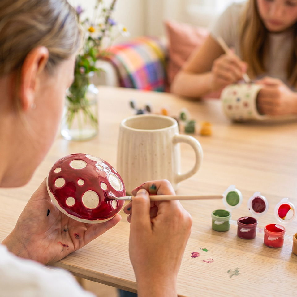 Child painting a red and white mushroom figurine with another child nearby.