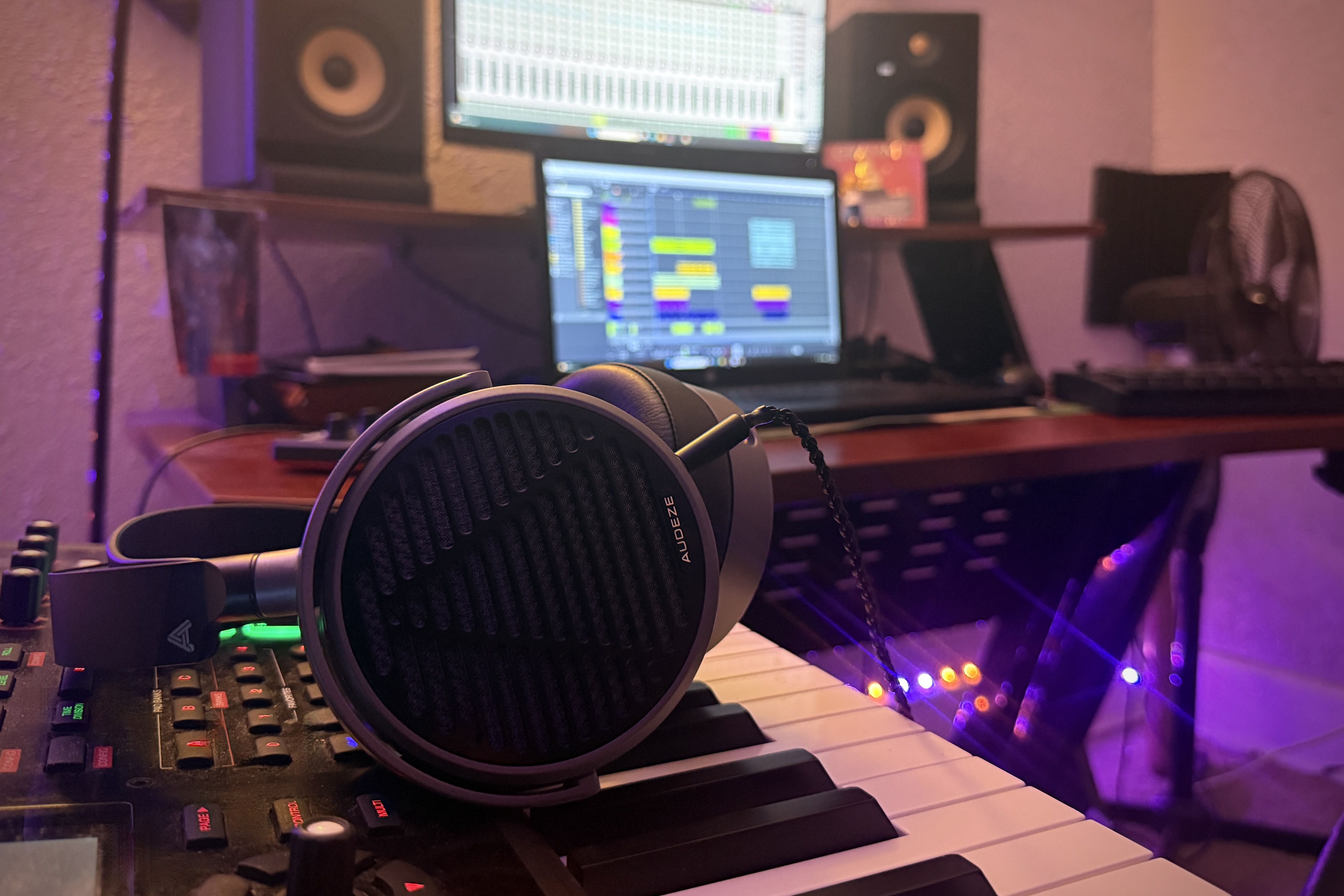 Audeze MM-100 Headphones on a keyboard with a computer screen and studio monitors in the background.