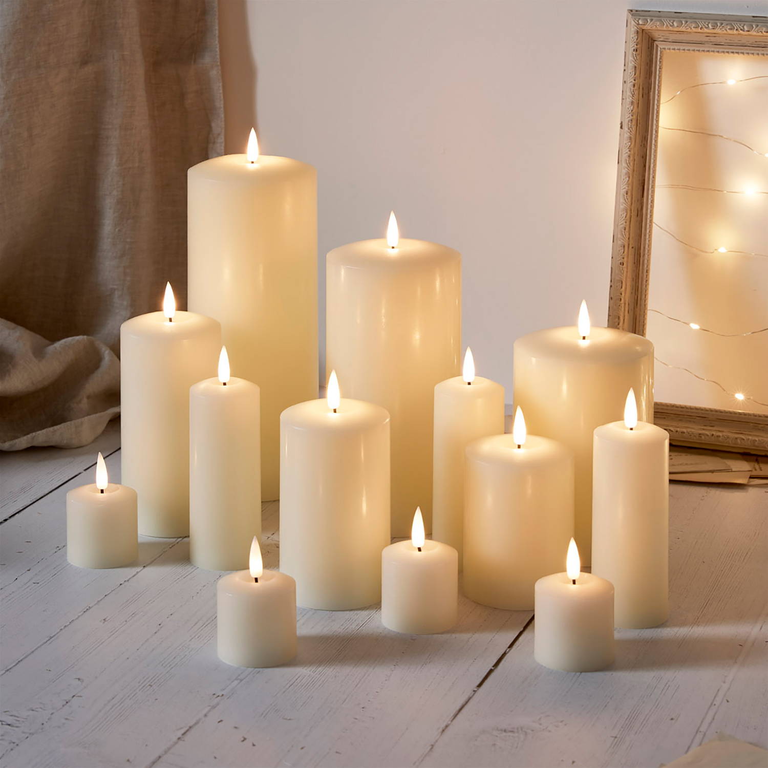 A collection of ivory LED candles on the floor with a mirror and fairy lights in the background.