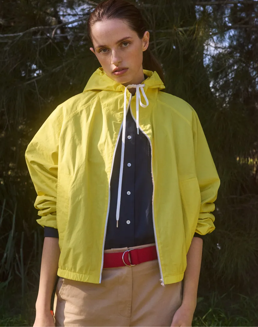 Model in a yellow jacket with a black shirt and red belt outdoors.