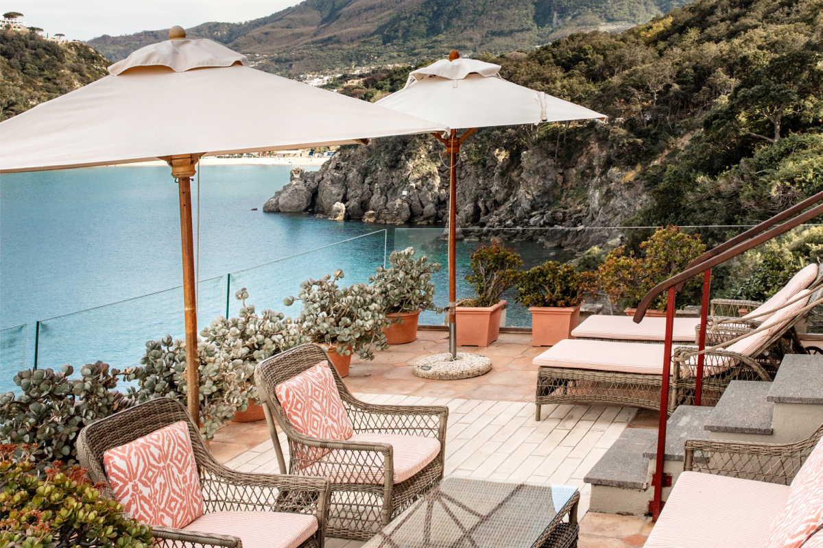 Vacation rental patio with outdoor umbrellas, lounge chairs, and woven seating overlooking a rocky coastline.