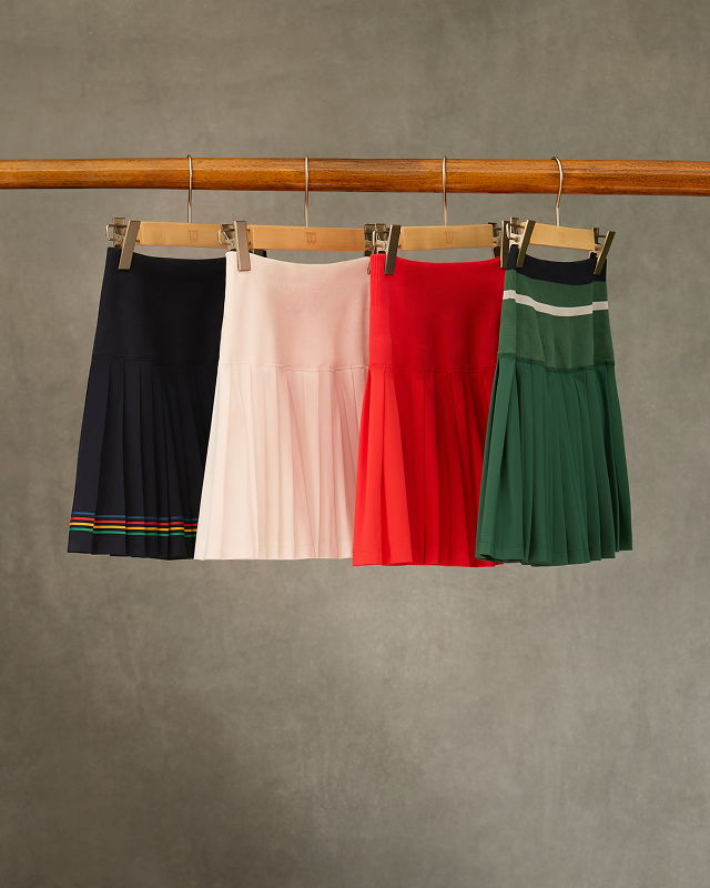 Four skirts hanging on a wooden rack with a gray background.