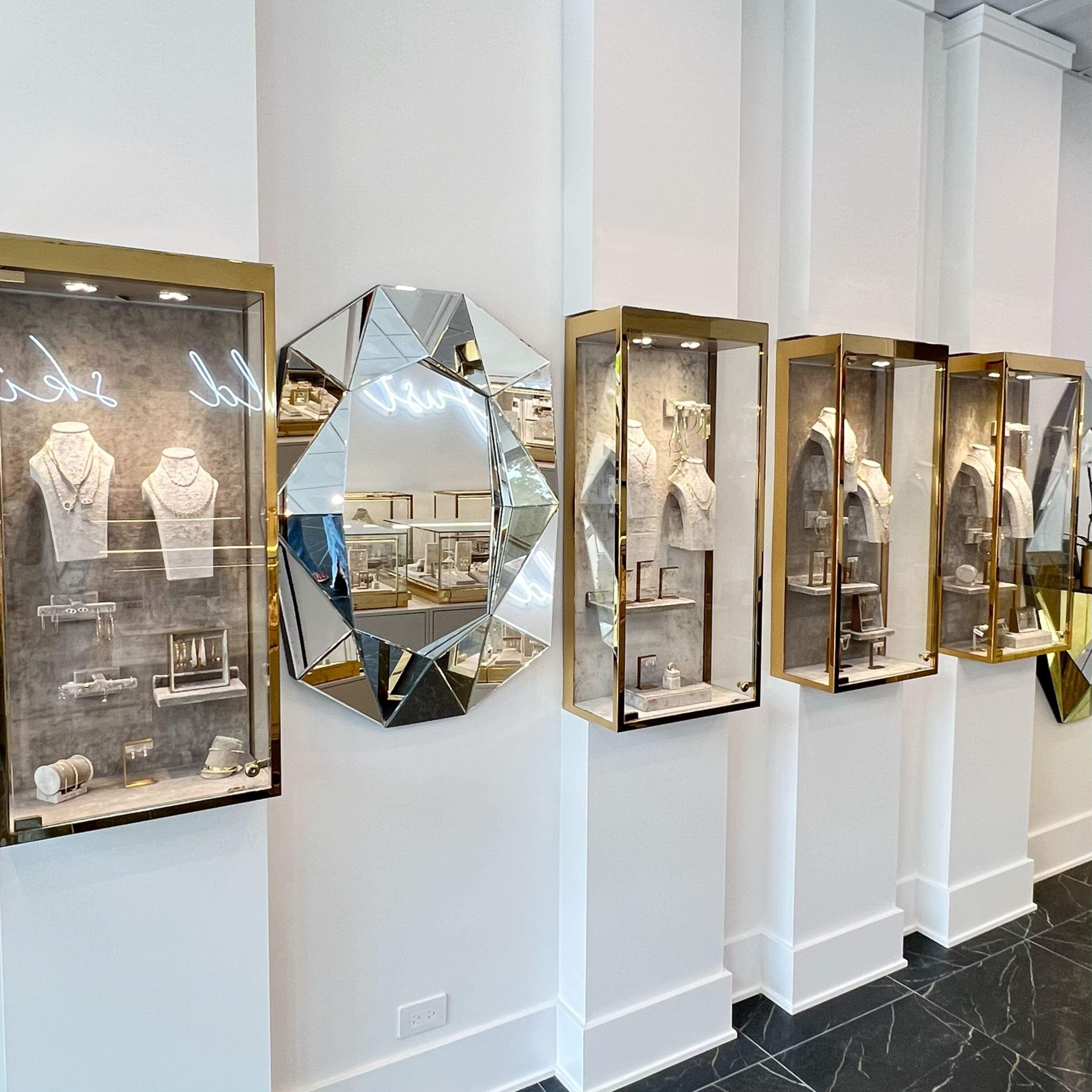Jewelry display cases on a white wall with diamond-shaped mirror.