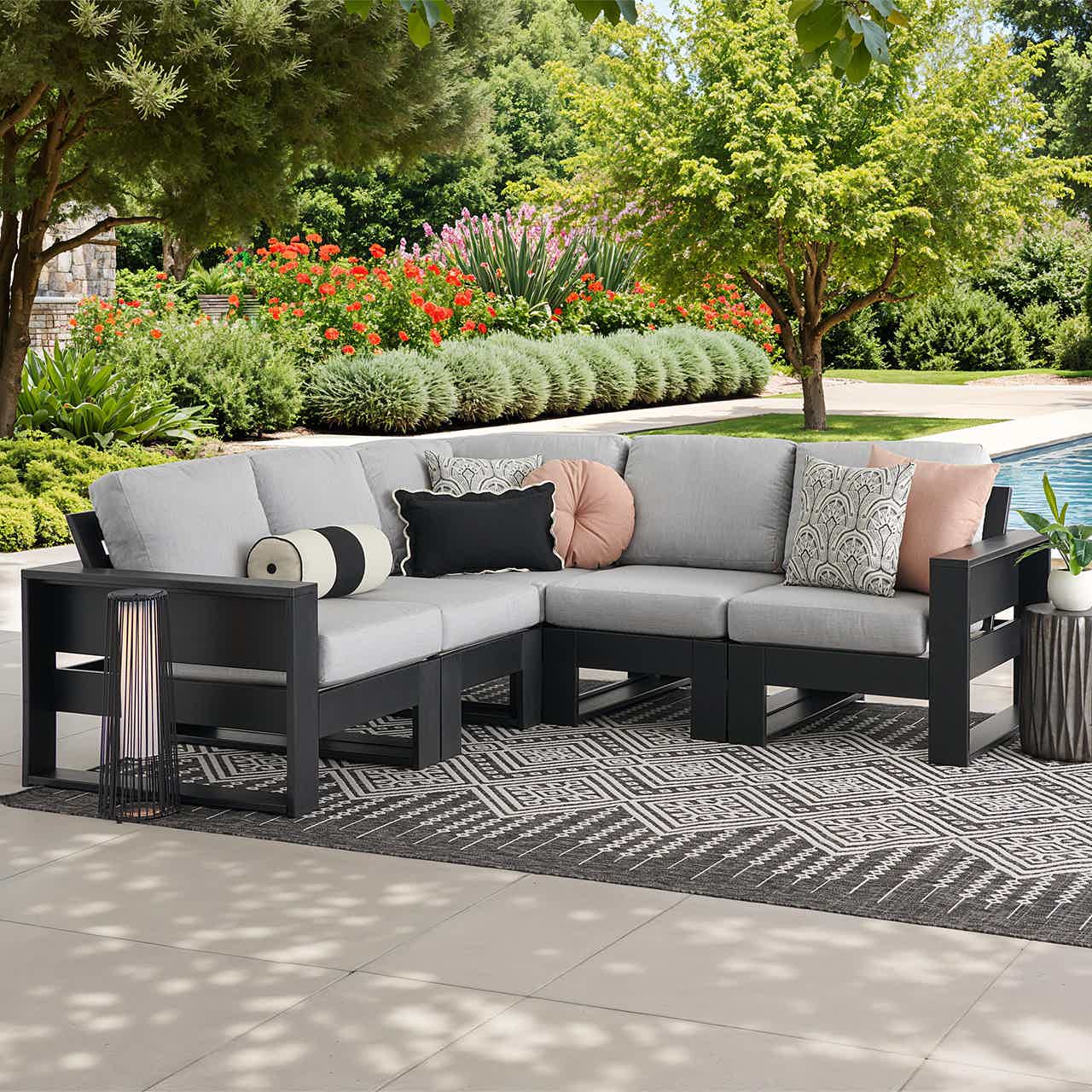 Outdoor sectional sofa with cushions, surrounded by greenery and a pool.