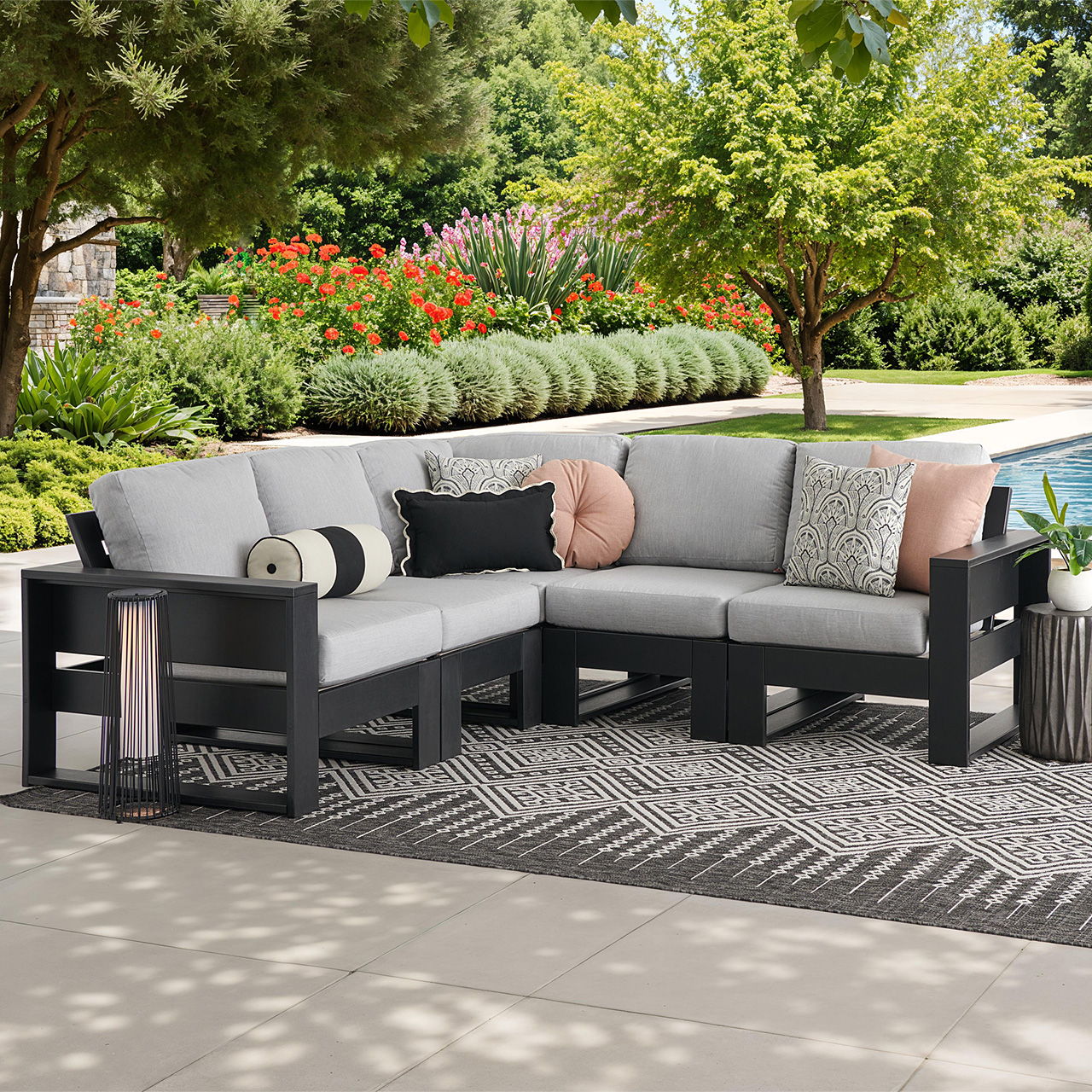 Outdoor sectional sofa with cushions, surrounded by greenery and a pool.