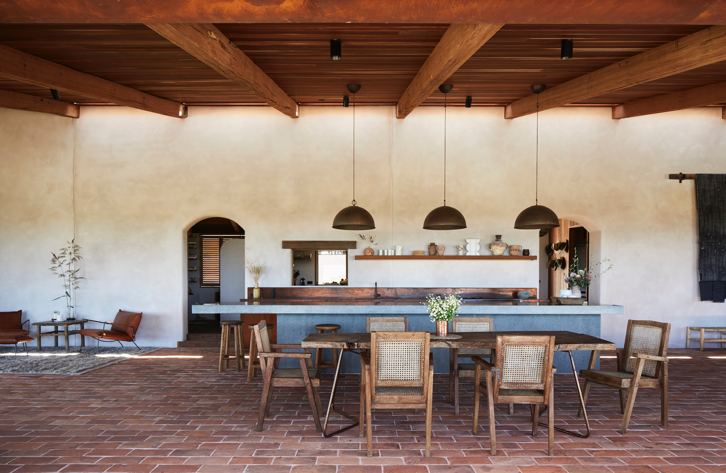 An open air outdoor kitchen area with metal pendant lights over a bench