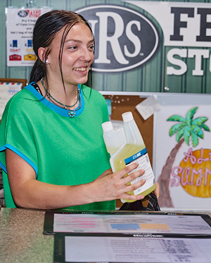 A young woman in a green shirt holding a bottle at a counter.