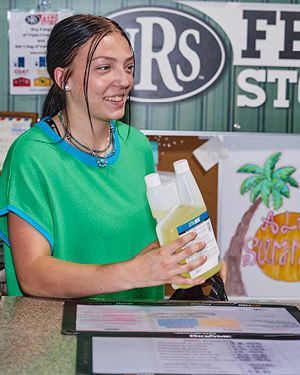 A young woman in a green shirt holding a bottle at a counter.