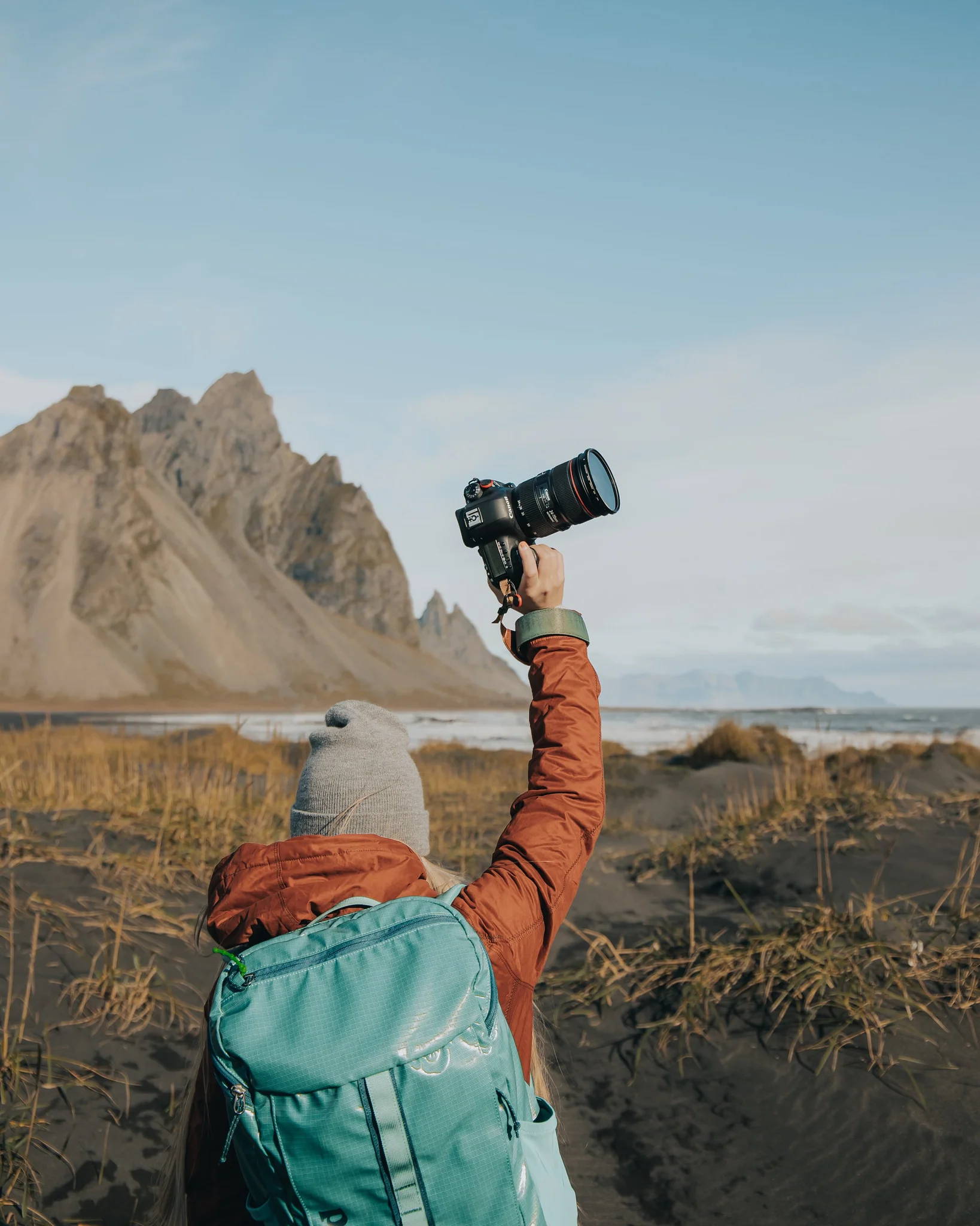 Woman holding a camera above her head in front of a nature background.