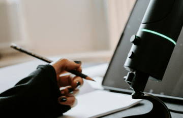 A hand holding a pen near a microphone and laptop.