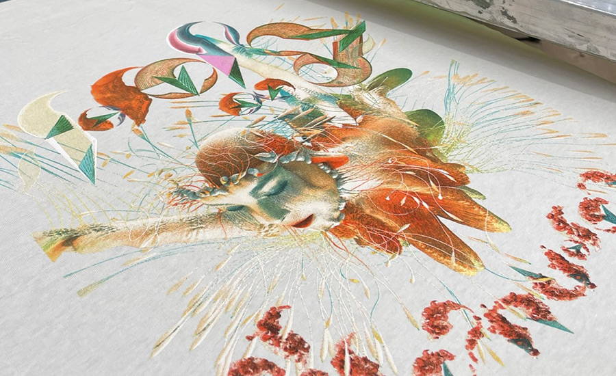 A simulated process screen print on a white shirt showing the use of halftones and blending to reproduce stunning detail and depth of a surrealist style artwork that features an etherial humanoid character blending into naturalistic elements and sprouting plantlike tendrils. The colours range features predominantly oranges and reds, with shading of shadow areas on the face in dark green torquoise tones and white highlights. There are geometric decorative character style elements above the creature that include an additional pink spot colour and decorative floral character style text elements below.