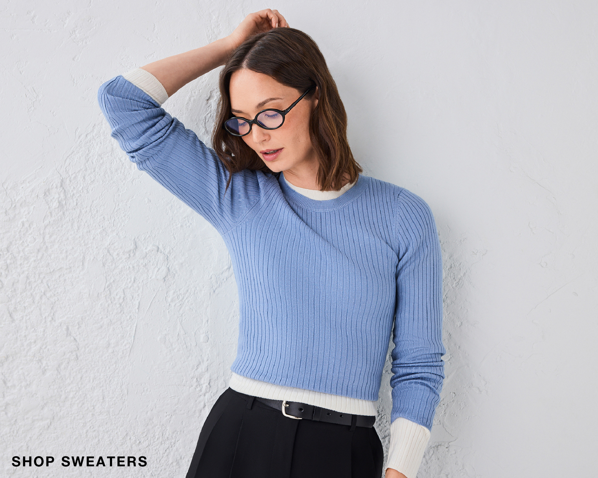 Woman wearing a light blue sweater and glasses against a white background.
